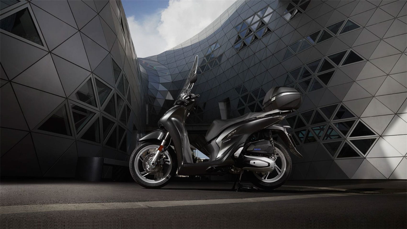 Σύγχρονο scooter Honda SH 125i μπροστά από μοντέρνο κτίριο, ιδανικό για leasing χωρίς προκαταβολή.